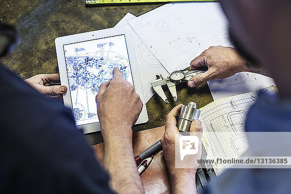 Hochwinkelansicht von Mechanikern mit einem Tablet-Computer während der Planung in einer Autowerkstatt