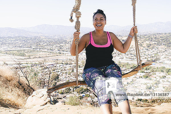 Cheerful woman swinging on rope swing against townscape
