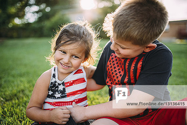 Happy boy tickling sister while sitting at backyard