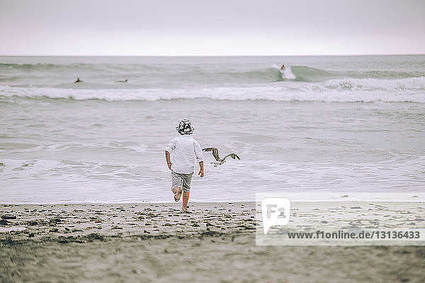 Rear view of boy running on sand at beach