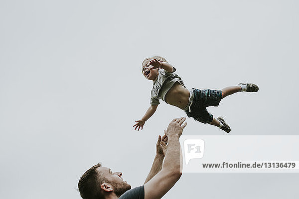 Verspielter Vater wirft Sohn gegen klaren Himmel in die Luft