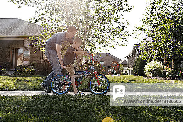 Vater hilft Sohn beim Fahrradfahren auf Straße gegen Himmel