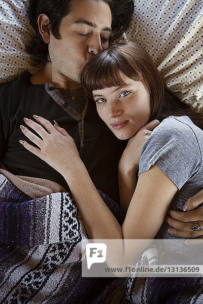 Mann küsst Frau auf die Stirn  während er im Wohnmobil auf dem Bett liegt