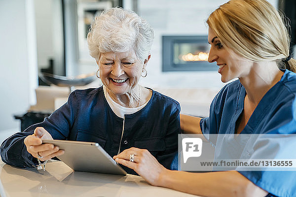 Glückliche ältere Frau  die einen Tablet-Computer mit einer häuslichen Pflegekraft benutzt