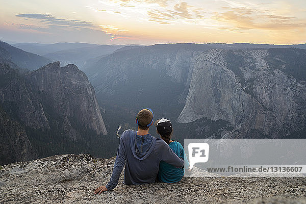 Rear view of couple sitting on mountain during sunset