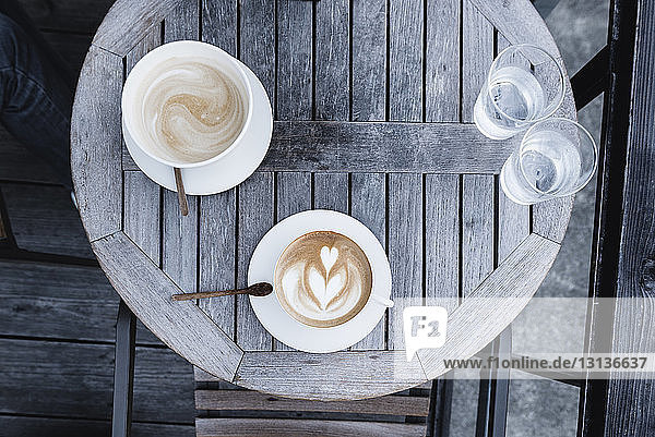 Draufsicht auf Kaffeetassen und Wassergläser auf Holztisch