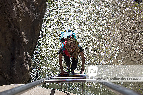 Portrait of female backpacker climbing ladder on sunny day