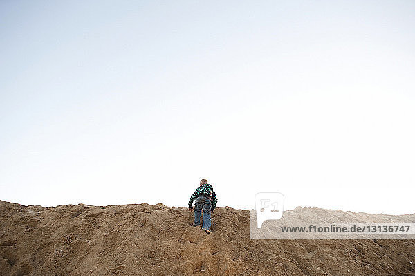 Rear view of boy climbing on sand dune at beach against sky
