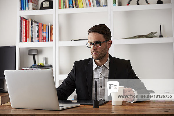 Geschäftsmann mit Laptop-Computer am Holztisch im Heimbüro