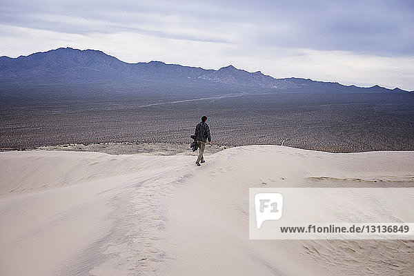 Rückansicht in voller Länge eines Mannes  der auf einer Sanddüne in der Wüste geht
