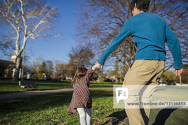 Rear view of daughter pulling father by holding his hands at park