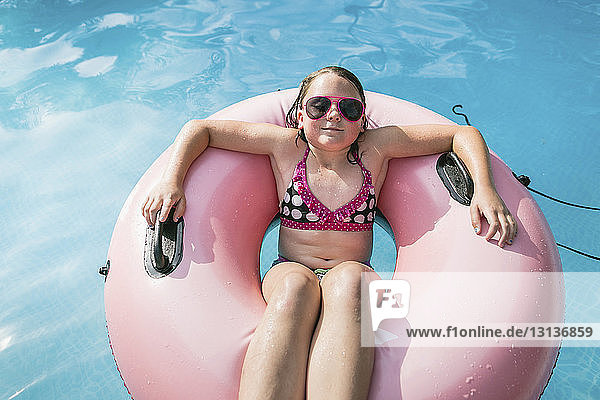 Hochwinkelaufnahme eines Mädchens mit Sonnenbrille  das auf einem aufblasbaren Ring im Schwimmbad ruht
