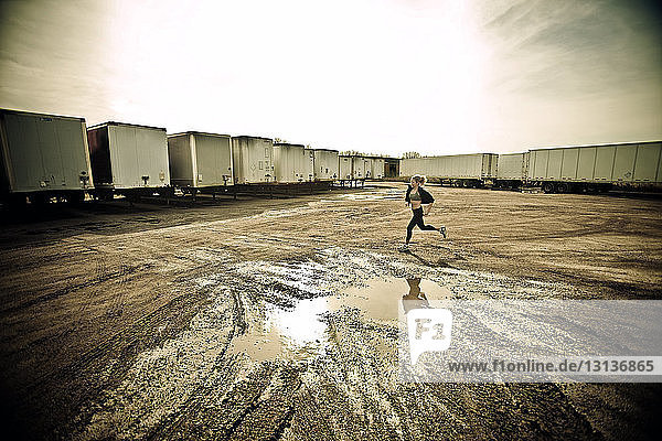 Athlete jogging on muddy field by cargo containers against sky