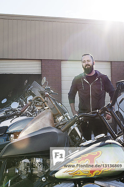 Selbstbewusster Mechaniker  der vor der Werkstatt bei den Motorrädern steht
