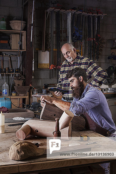 Senior man looking at worker carving wood at workshop
