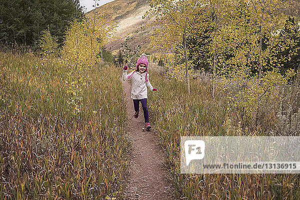 Girl walking on trail amidst grassy field during autumn