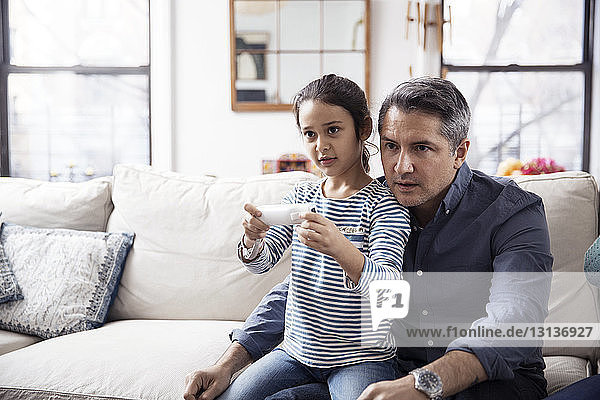 Girl playing video game while sitting with father at home