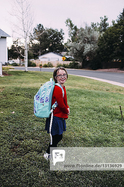 Porträt eines auf dem Rasen stehenden Mädchens mit Rucksack