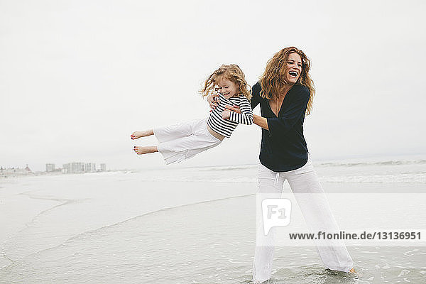 Glückliche Mutter dreht Tochter  während sie im Meer vor klarem Himmel am Strand steht
