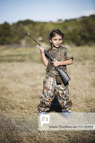 Portrait of confident girl holding rifle on grassy field
