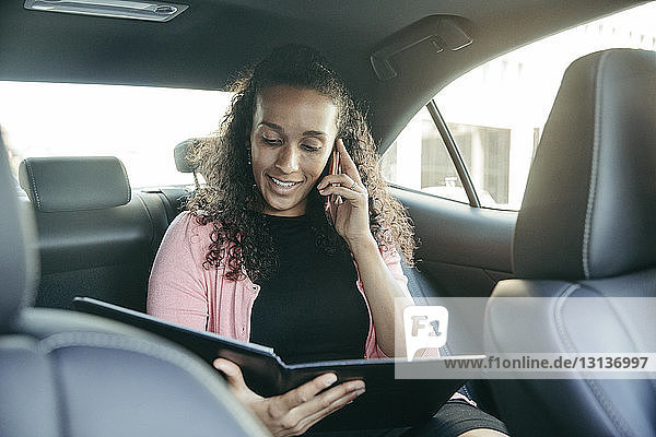 Geschäftsfrau sieht sich Datei an  während sie im Auto mit einem Smartphone telefoniert