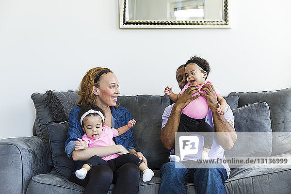 Glückliche Eltern spielen mit ihren Töchtern  während sie auf dem Sofa sitzen