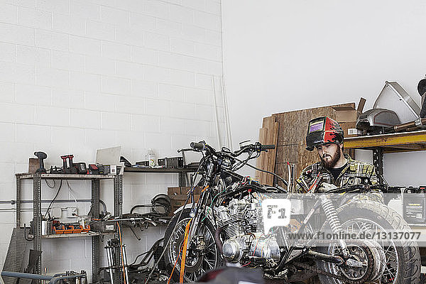 Seriöser Mechaniker  der in einer Autowerkstatt am Motorrad arbeitet
