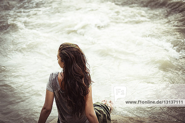 Hochwinkelaufnahme einer Frau  die auf einem Felsen gegen einen Fluss sitzt