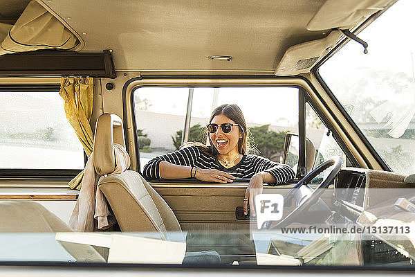 Fröhliche Frau lehnt im Urlaub am Fenster eines Kleinbusses