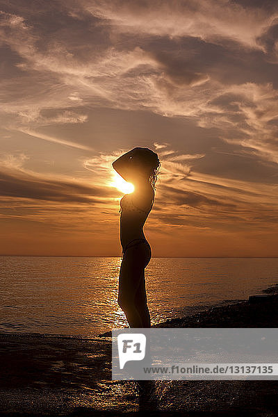 Seitenansicht der Silhouette einer sinnlichen Frau  die bei Sonnenuntergang am Strand steht