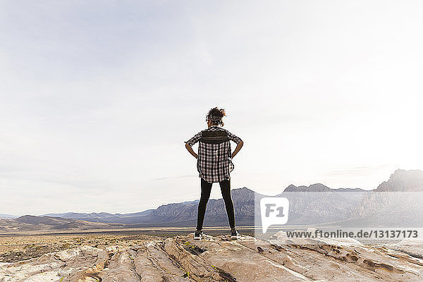 Rear view of woman looking at view while standing on rock formation against clear sky