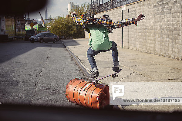 Rear view of man performing skateboard stunt over barrel on street
