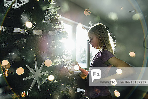 Seitenansicht eines Mädchens  das zu Hause am beleuchteten Weihnachtsbaum steht