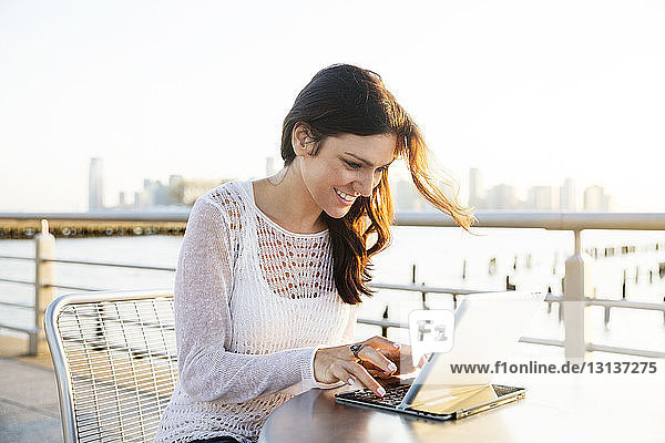 Glückliche Frau mit Tablet-Computer im Café an der Promenade bei Sonnenuntergang