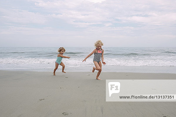 Glückliche Schwestern spielen am Cape May Beach gegen Himmel und Meer