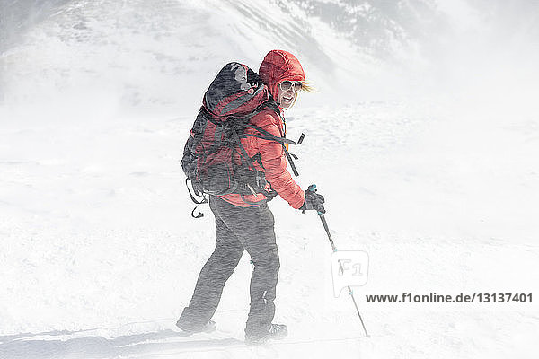 Hochwinkelaufnahme einer Wanderin mit Rucksack mit Wanderstöcken während eines Schneesturms