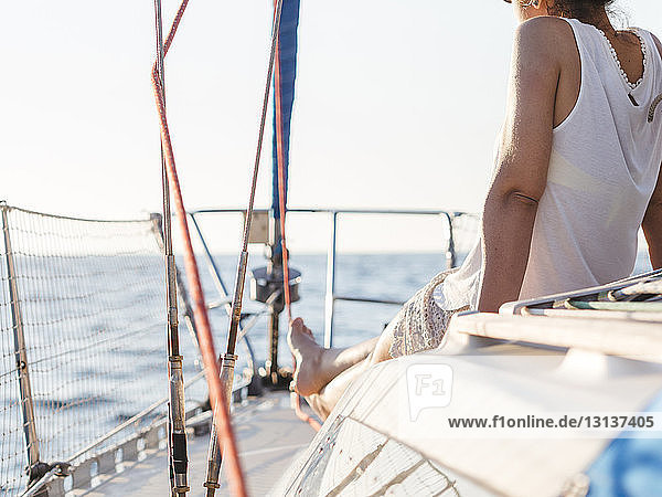 Low section rear view of woman sitting in sailboat against clear sky