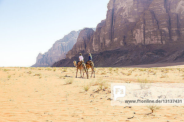 Friends riding on camel in desert against clear sky
