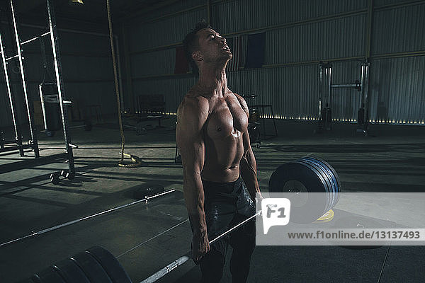 Männlicher Athlet ohne Hemd beim Hantelheben im Fitnessstudio