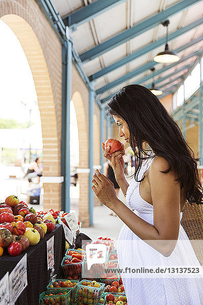 Seitenansicht einer Frau  die beim Einkauf auf dem Markt an Tomaten riecht