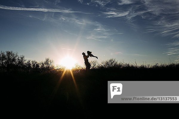 Silhouette father lifting daughter while playing with her on field against sky during sunset