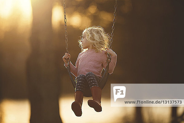 Girl playing on swing at playground during sunset