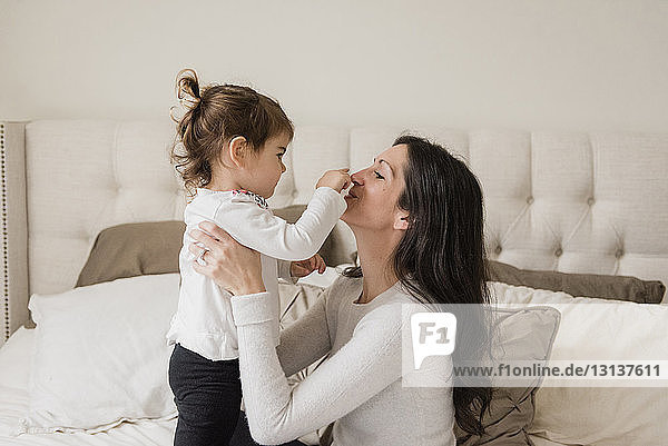 Seitenansicht der Tochter  die beim Spielen zu Hause die Nase der Mutter berührt
