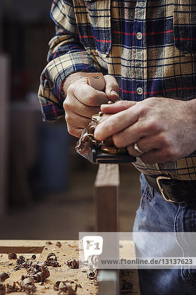 Mittelteil eines Arbeiters beim Rasieren eines Holzbretts in der Werkstatt