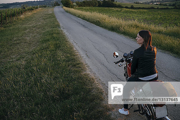 Hochwinkelaufnahme einer Motorradfahrerin  die auf einem Motorrad auf einer Landstraße sitzt