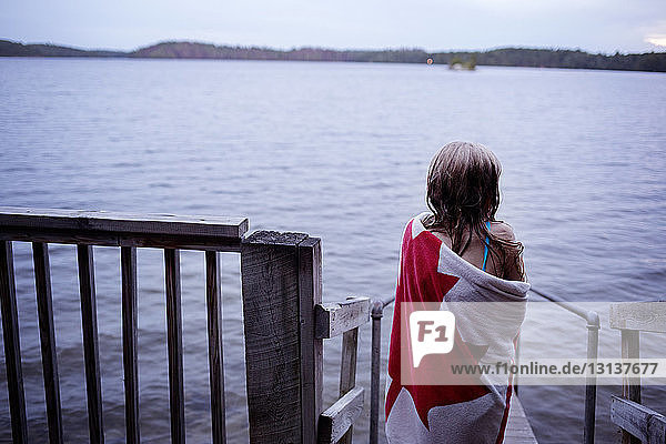 Rear view of girl wrapped in towel standing on jetty over lake