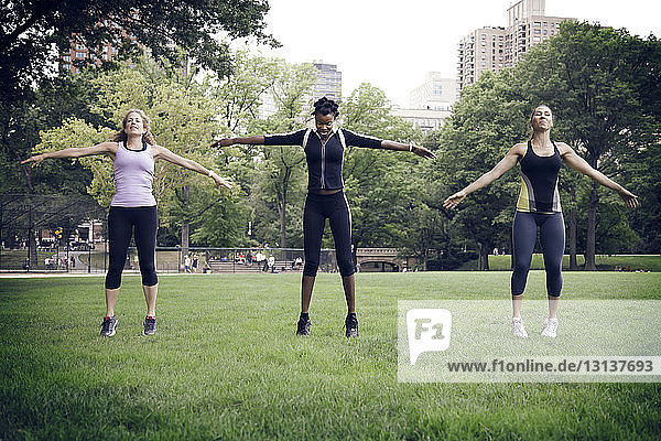 Female athletes with arms outstretched exercising on field at park