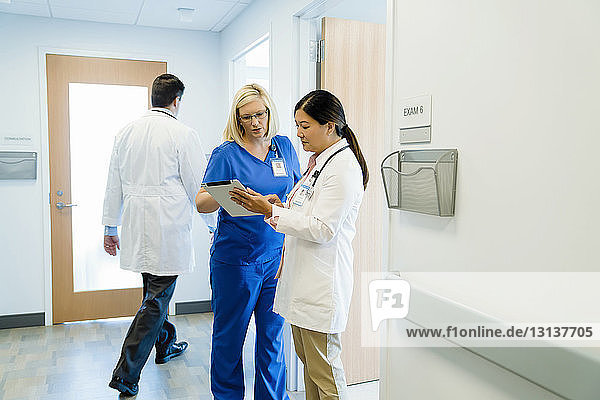 Female doctors discussing over tablet computer with male colleague walking in background