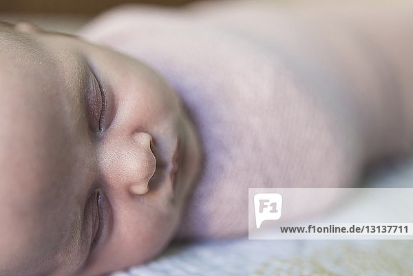 Close-up of baby girl sleeping while being wrapped in blanket