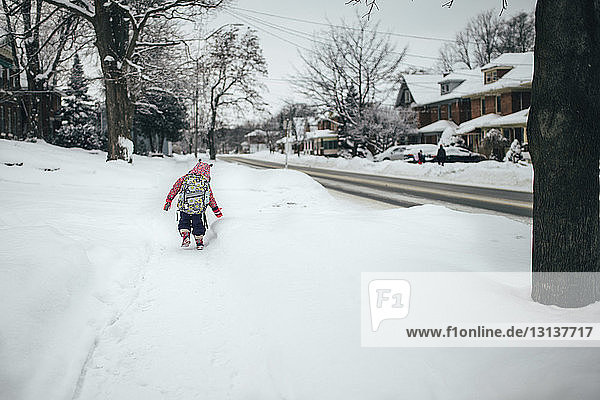 Rückansicht eines Jungen mit Rucksack  der auf einem schneebedeckten Feld läuft